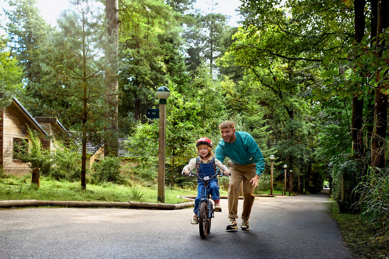 Father helping a girl learn to ride her bike in the forest.